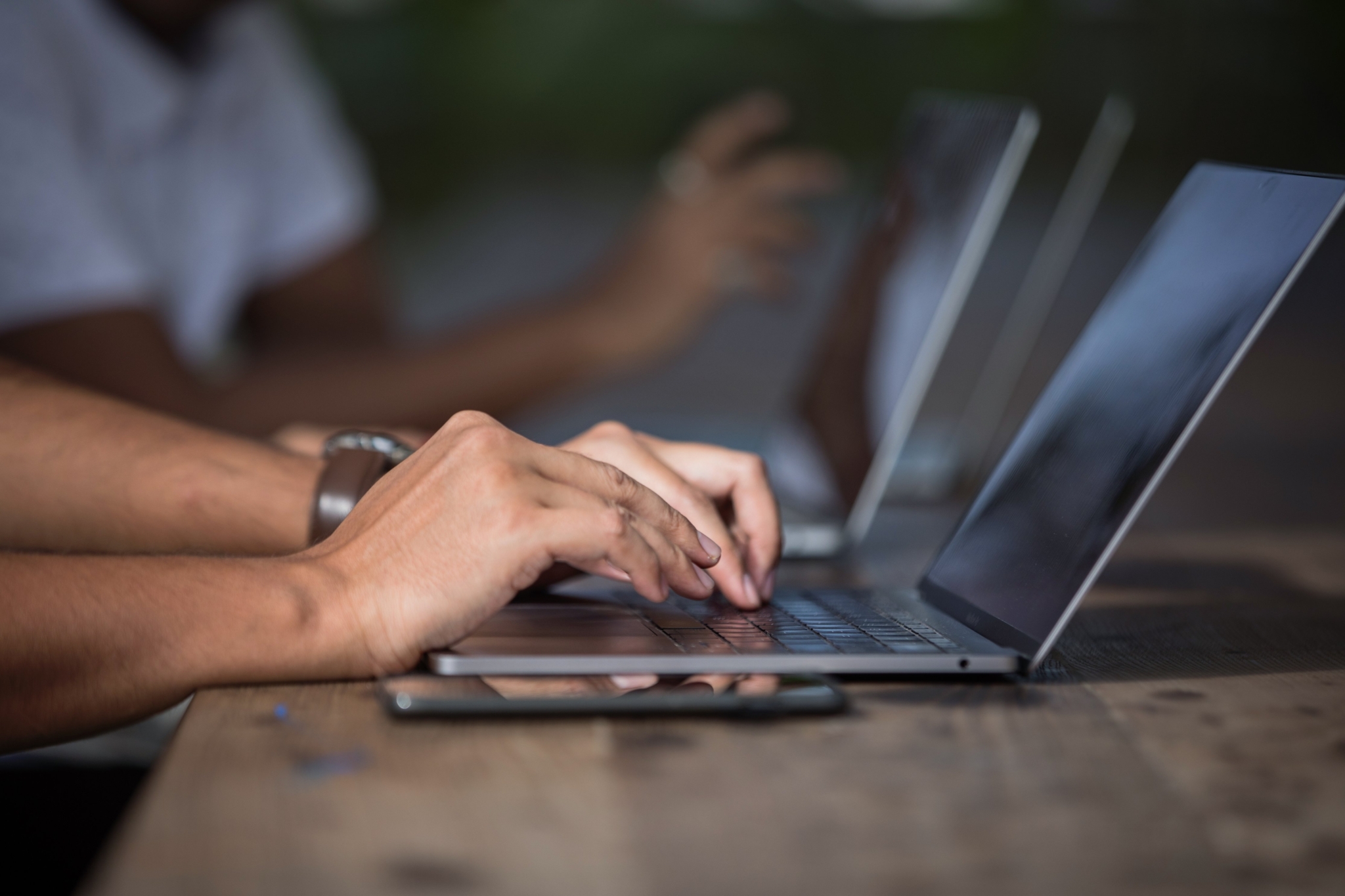 Two hands typing on a laptop that is sitting on a brown, wood-panelled desk