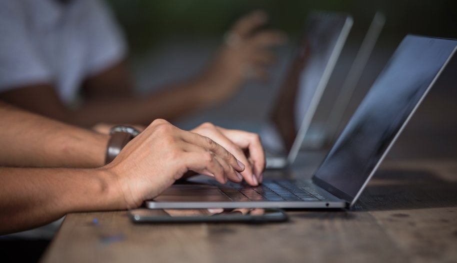 Two hands typing on a laptop that is sitting on a brown, wood-panelled desk