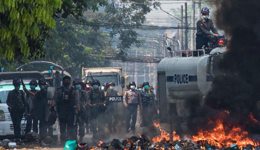 Security forces gather behind a burning barricade during a crackdown on protests against the military coup in Yangon on March 17, 2021. (Photo by STR / AFP) (Photo by STR/AFP via Getty Images)