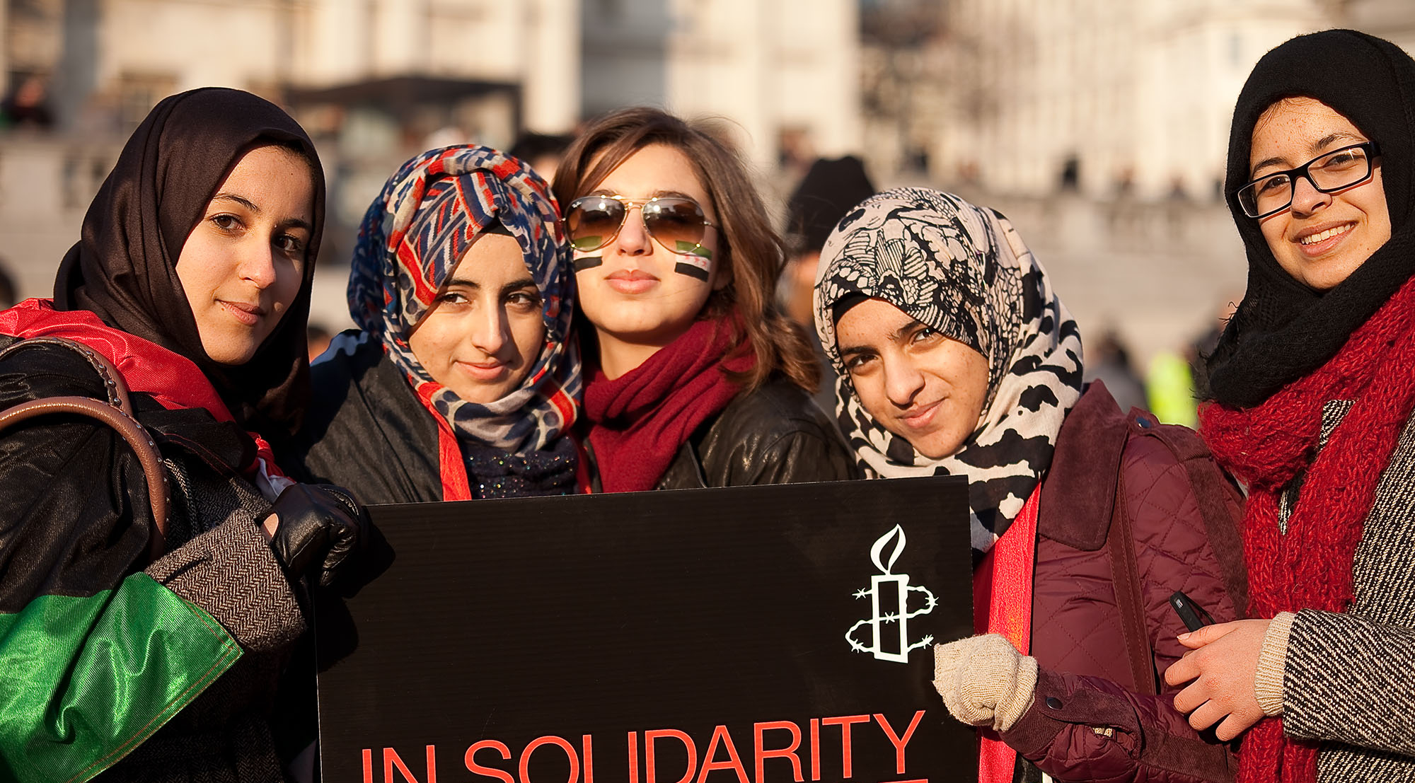 5 women at international women's day march holding an "In Solidarity in Defiance" Amnesty sign