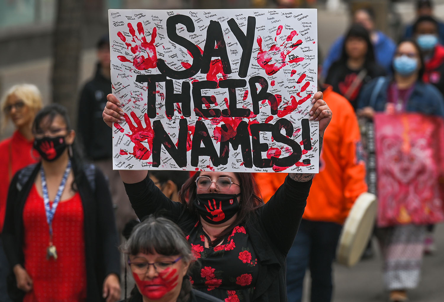 A protest with a women holding up a sign that reads "Say their names"