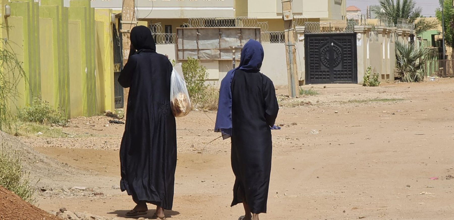 Women carrying shopping bags walk on an empty street in Khartoum's Jabra neighbourhood. Photo by AFP via Getty Images.