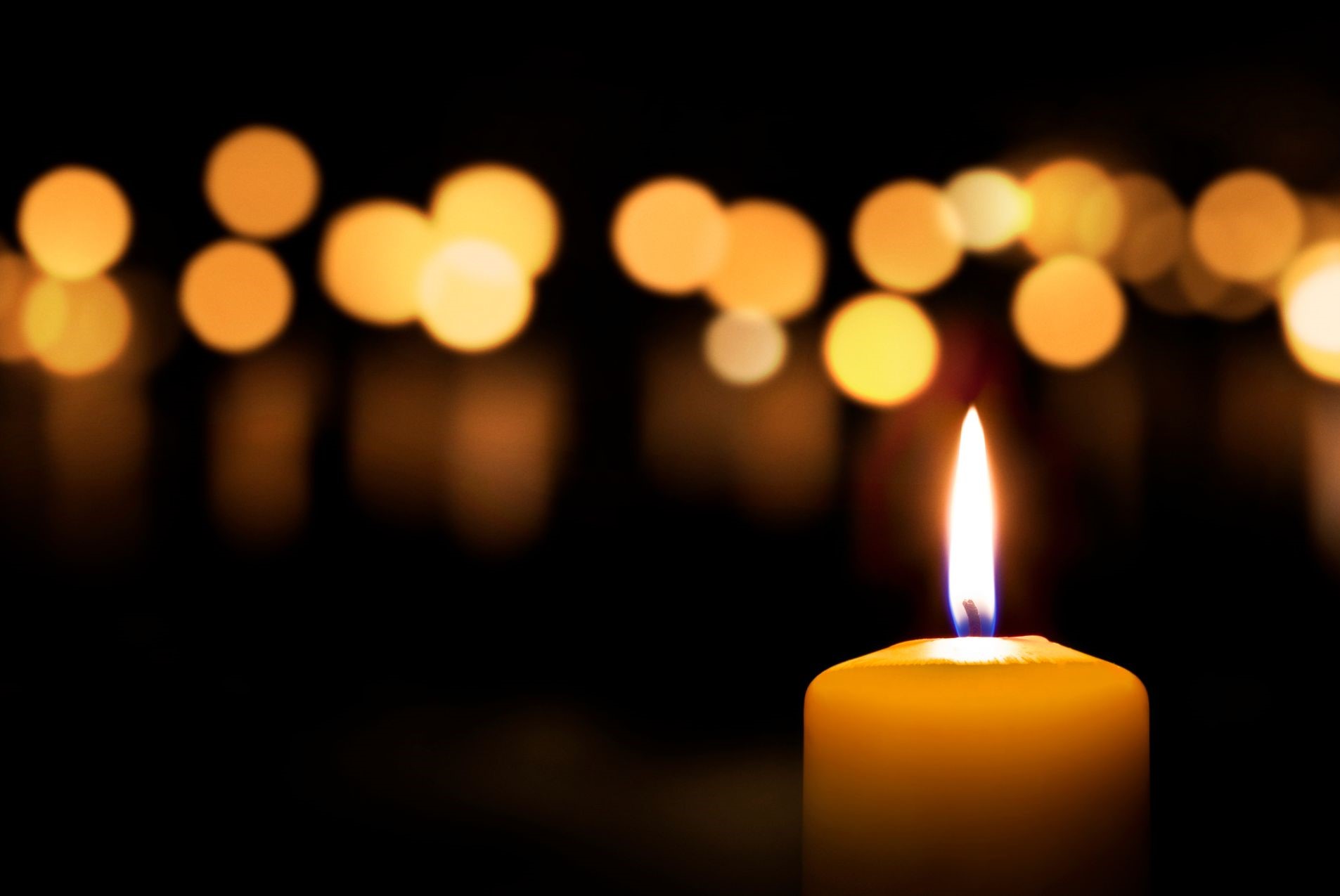 A candle in the dark with candle lights blurred out in the background