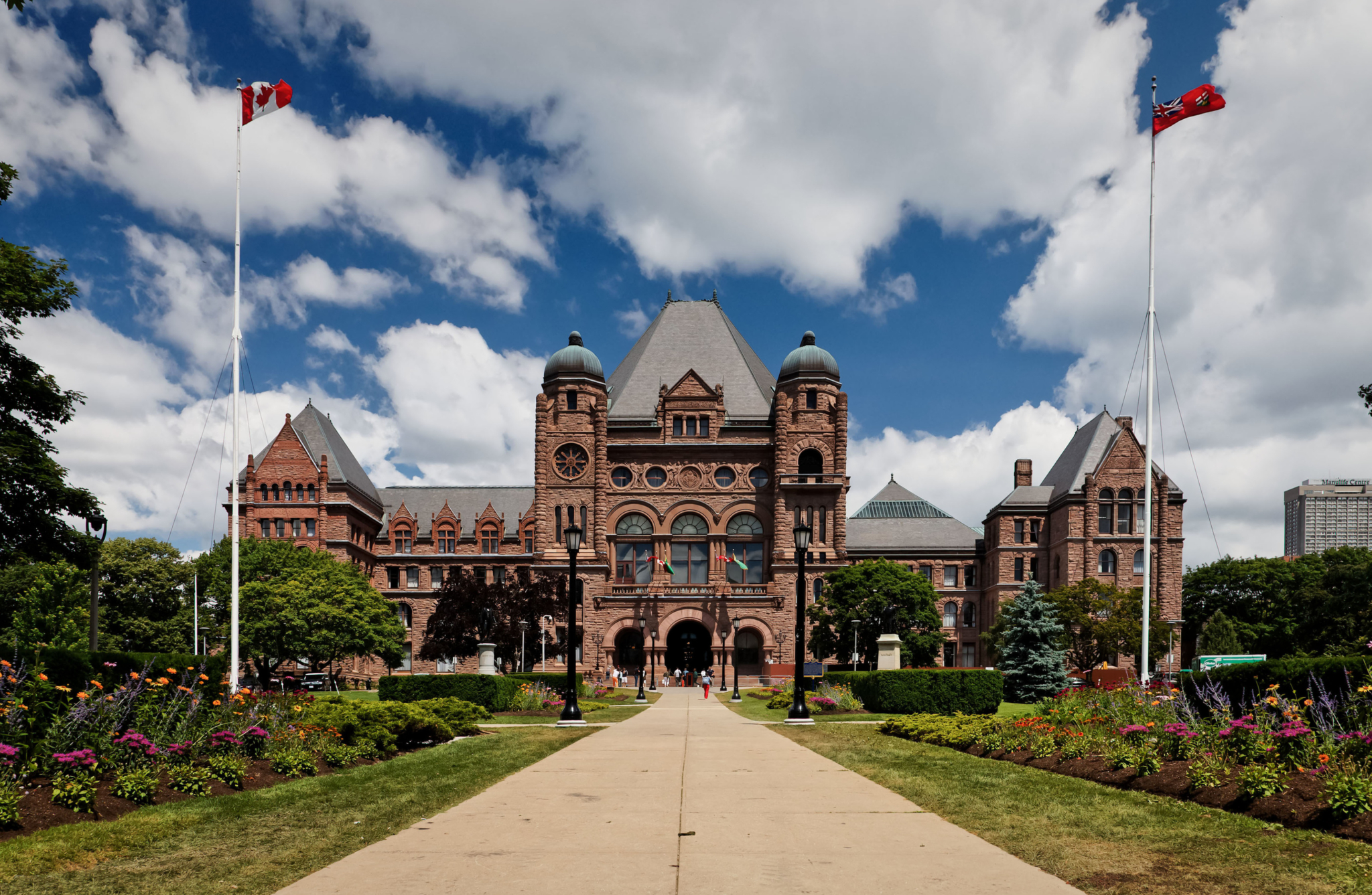A neo-Romanesque building with pink stone on a brightly, partly cloudy day