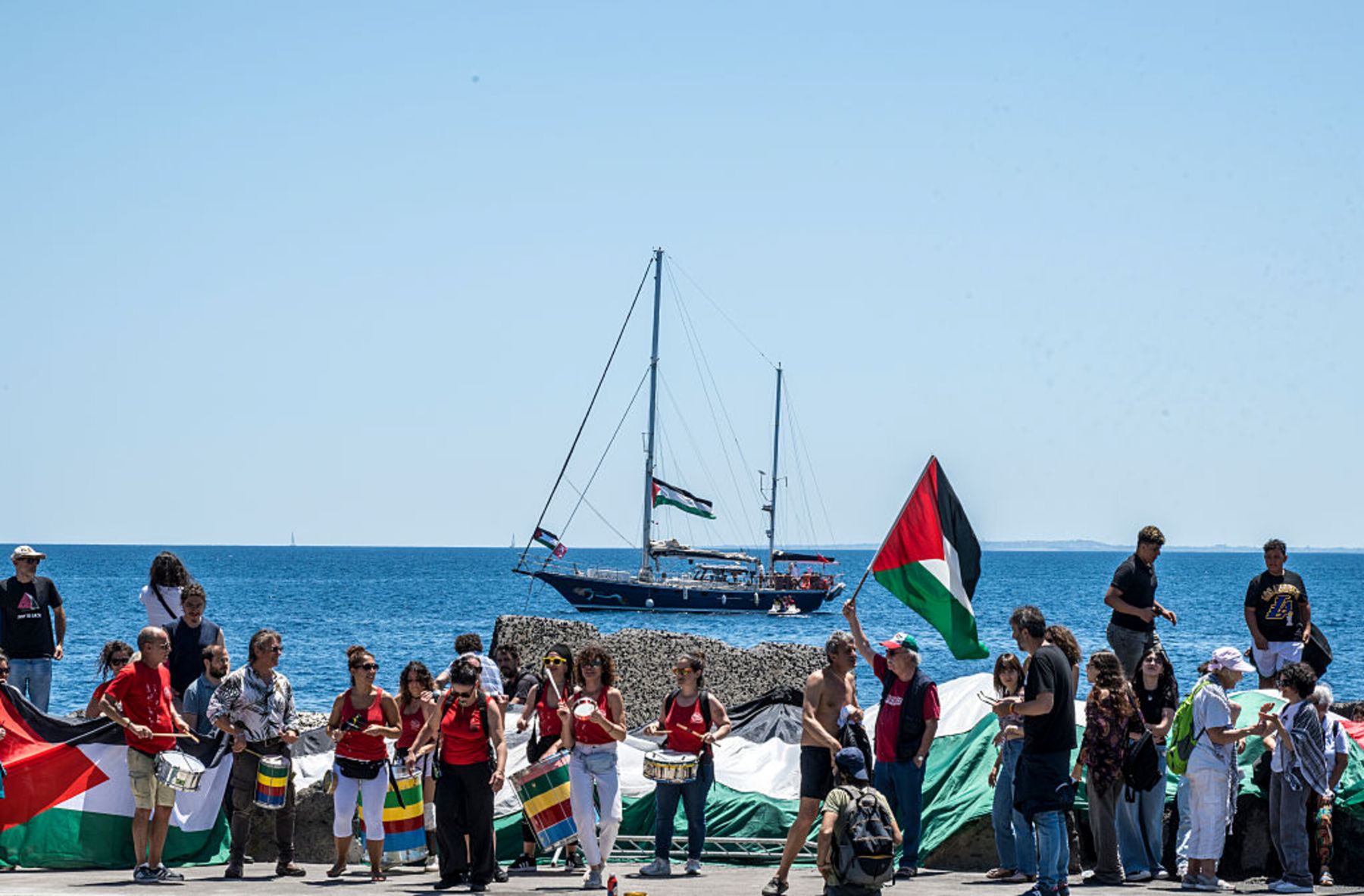 On the quay of San Giovanni Li Cuti, a group of activists attend the departure of the Madleen for Gaza with songs and Palestinian flags on June 01, 2025 in Catania, Italy. Photo by Fabrizio Villa/Getty Images.