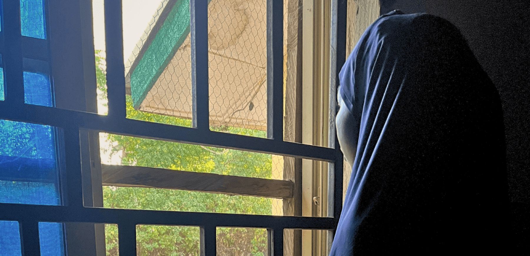 young woman with a headscarf looking out the window by Amnesty International.