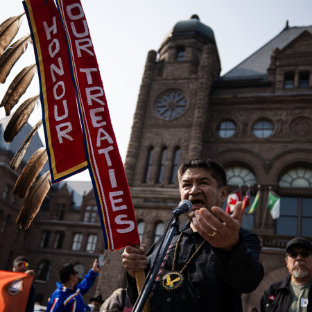 Indigenous man at a rally with sign reading "Honour Our Treaties"