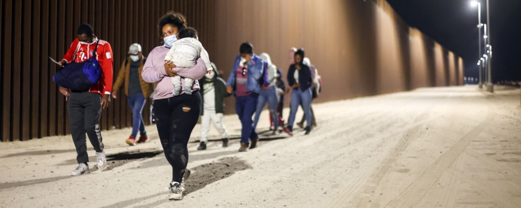 Immigrants walk along the U.S.-Mexico border barrier in the early morning hours on their way to be processed by the U.S. Border Patrol, after crossing from Mexico, on May 23, 2022 in Yuma, Arizona. Photo by Mario Tama/Getty Images.