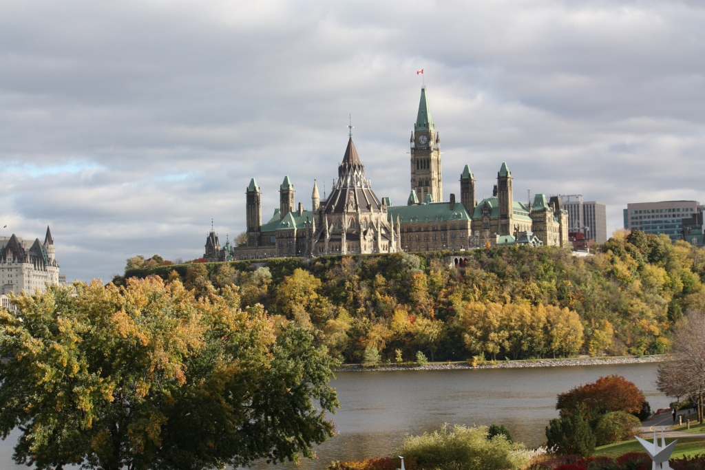 A collection of Gothic Revival buildings on a tree-lined hill over-looking a river on a cloudy day