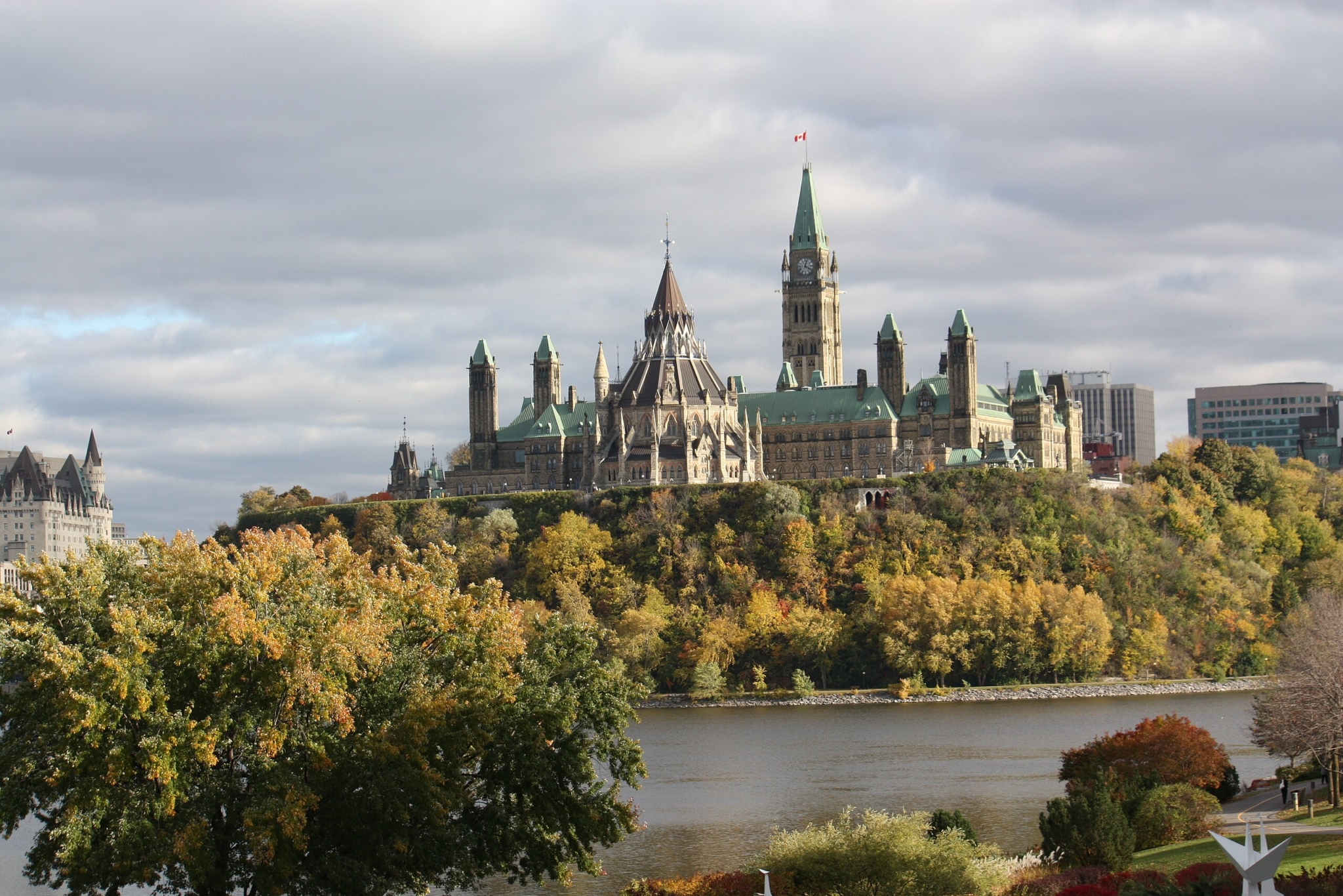 A collection of Gothic Revival buildings on a tree-lined hill over-looking a river on a cloudy day