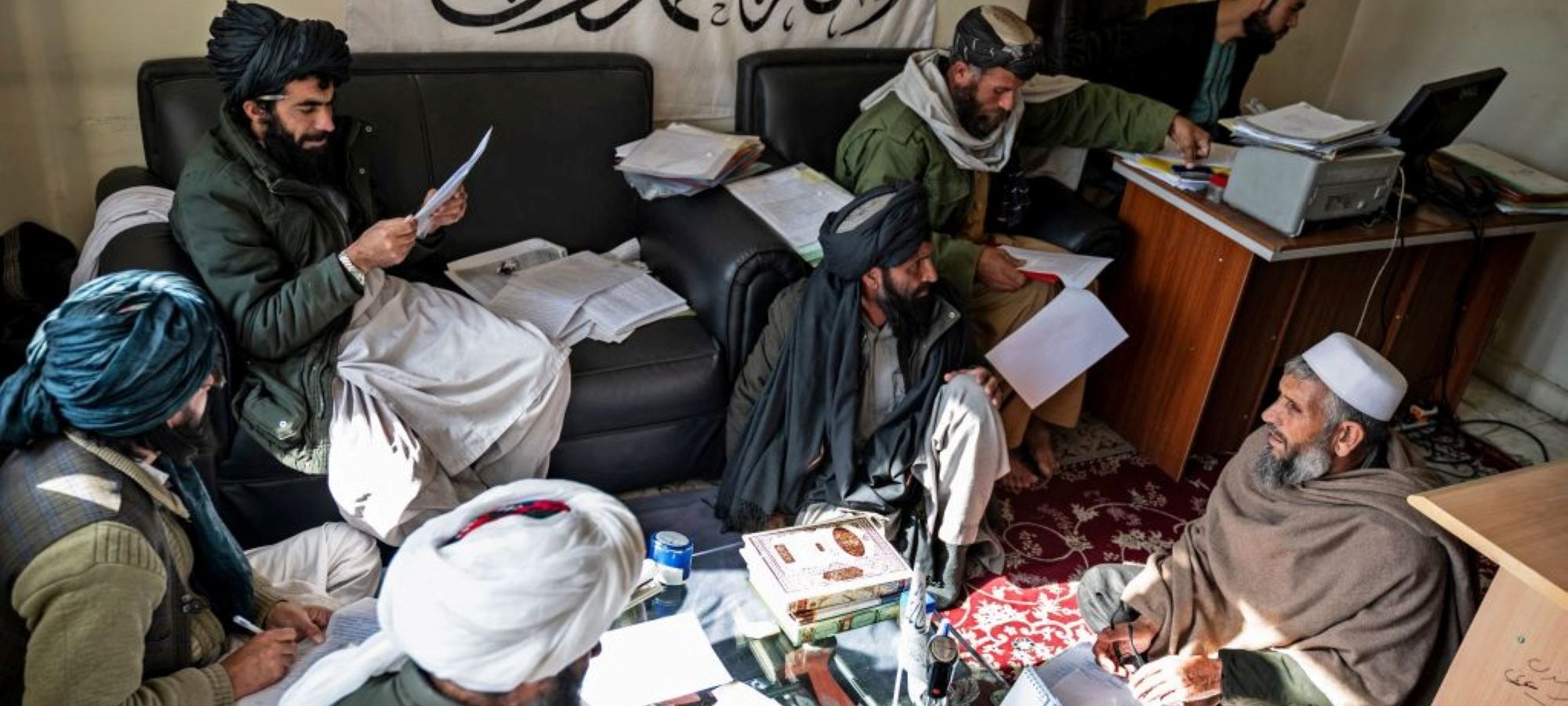 On November 28, 2022, judges (L) from the civil court check documents from the case of a petitioner at the Ghazni Court of Appeal in Ghazni, eastern Afghanistan. Kneeling in front of a turbanned judge in a tiny room at the Ghazni Court of Appeal in eastern Afghanistan, an old man sentenced to death for murder pleads for his life. Photo by WAKIL KOHSAR/AFP via Getty Images.