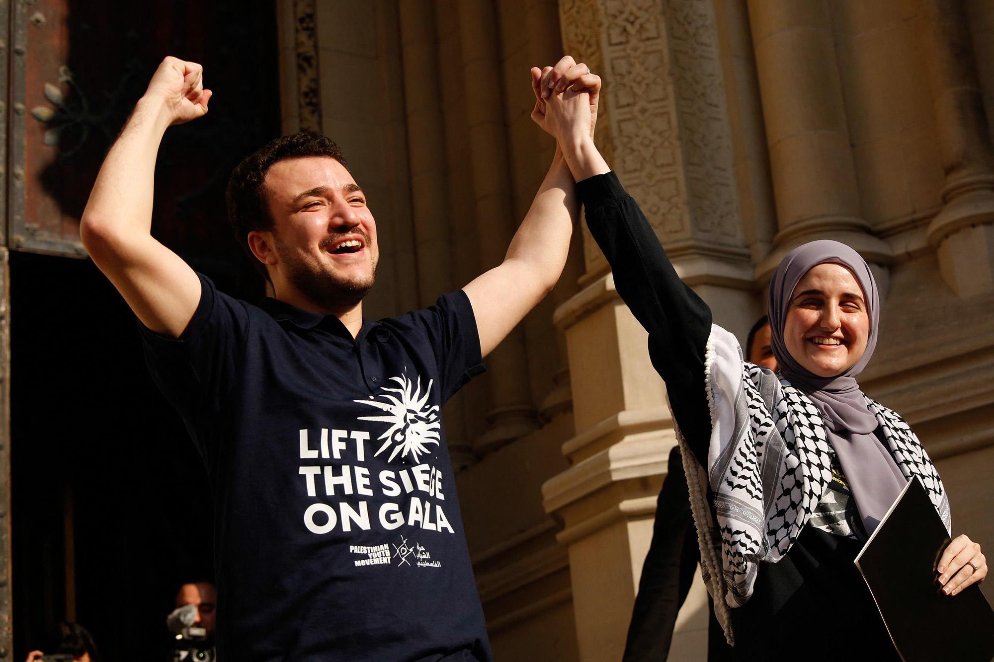 A may in joy with his arms up in the air celebrating while holding his wife's hand