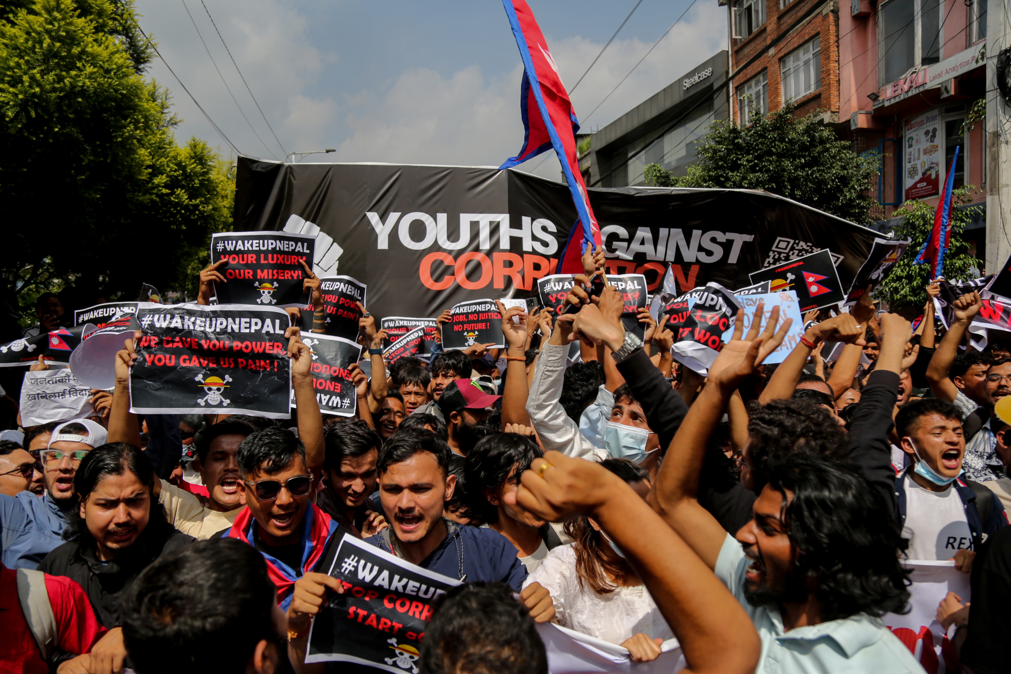 A group of people march outside holding signs decrying the Nepal government.