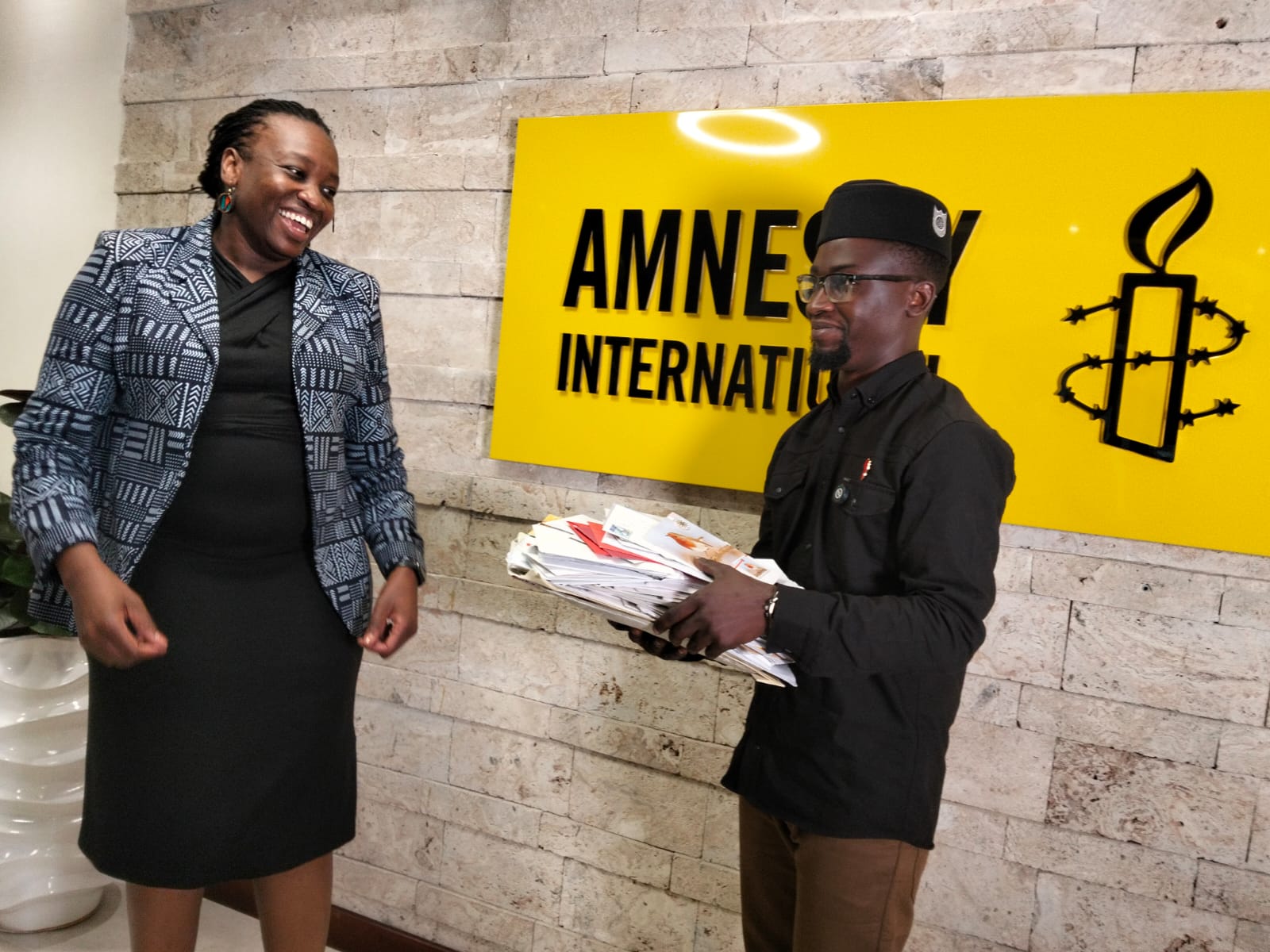 King Mwamisyo Ndungo holding a bunch of solidaity letters in his hands in front of an Amnesty International banner. There's a woman standing to his left smiling
