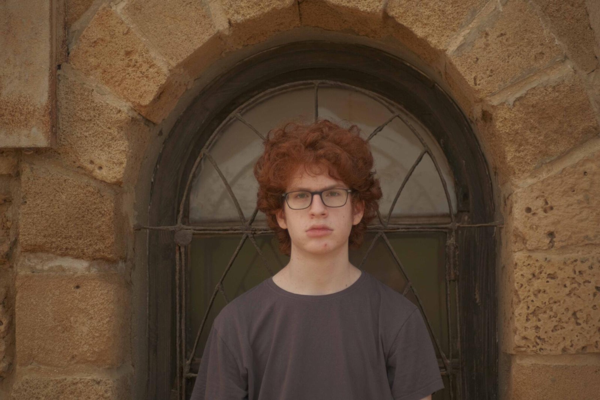 A young man wearing a grey tshirt and glasses looks into the camera