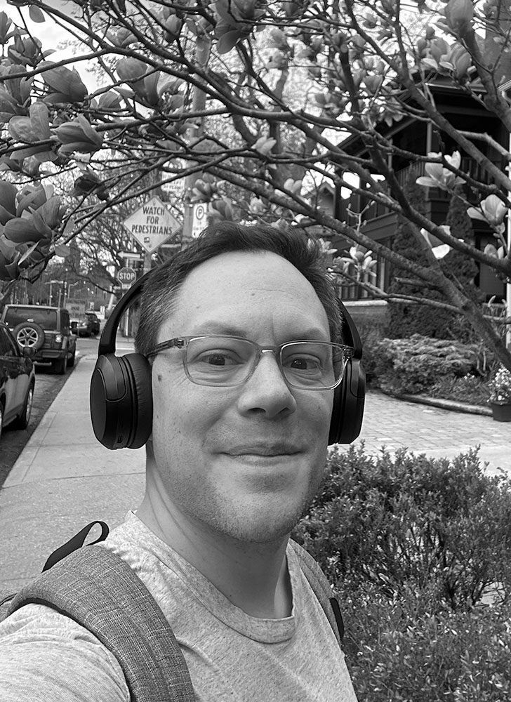 Cory Ruf smiling with headphones on in front of a tree with buds on it.