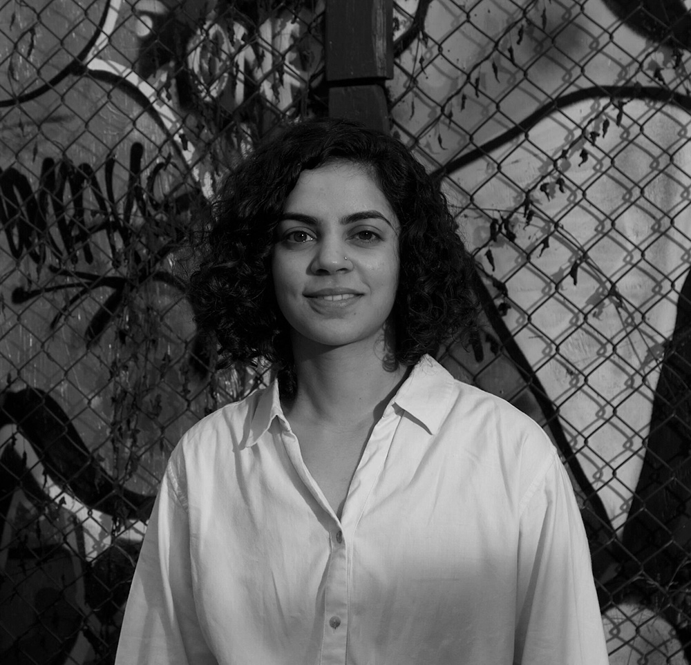 Sharon Nadeem standing in front of a fence with graffiti behind it.