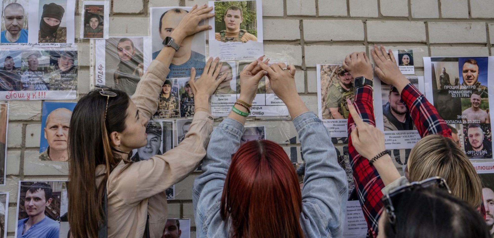 People stick up portraits of their missing or captured relatives and friends during the arrival of freed injured and severely wounded Ukrainian POWs in the Chernygiv region after a prisoners exchange on June 10, 2025. Photo by ANDREW KRAVCHENKO/AFP via Getty Images.