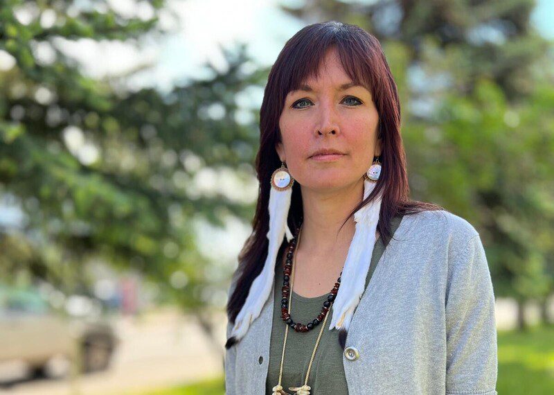 Molly (aka Sleydo') looks defiantly at the camera. She is a red haired woman wearing long earrings and a beaded necklace.