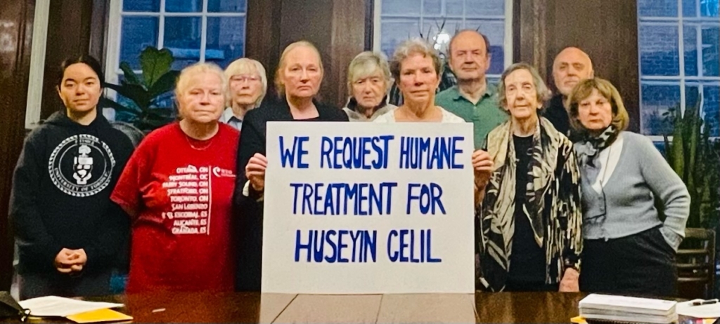 A group of people standing behind a square placard that reads "we request humane treatment for Huseyin Celil"