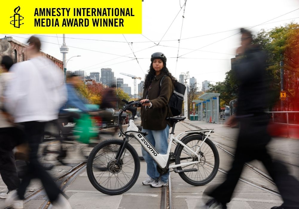 A woman standing with her bike in the middle of a crosswalk in Toronto while pedestrians cross the street blurred out